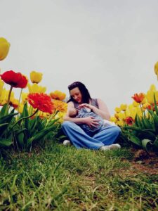 Kat breastfeeding daughter outdoors amongst the flowers