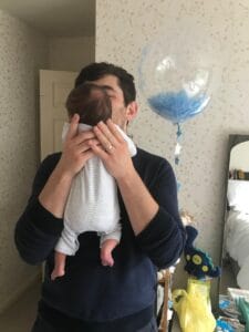 New dad holding baby son with blue balloon in background
