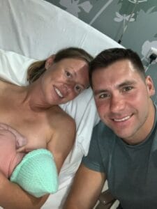 New mum breastfeeding in hospital bed with husband beside her